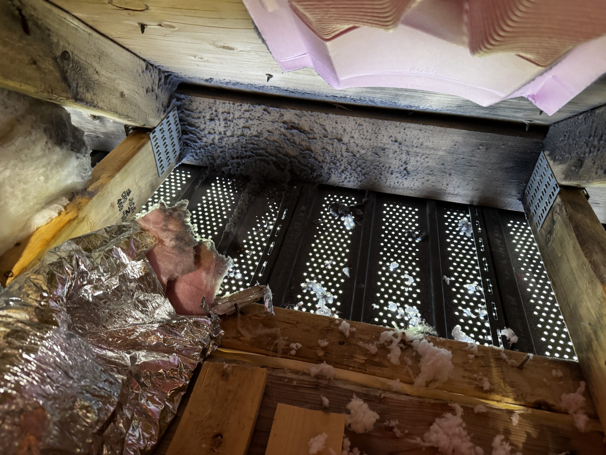 Attic view showing unvented soffit area with insulation and lint buildup